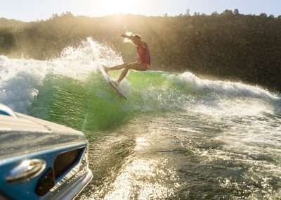 Person wakeboarding on sunlit wave behind boat